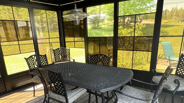 Un patio couvert avec une table et des chaises en métal, de grandes fenêtres et une terrasse en bois.