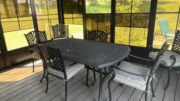 Un patio couvert avec une table et des chaises en métal, de grandes fenêtres et une terrasse en bois.