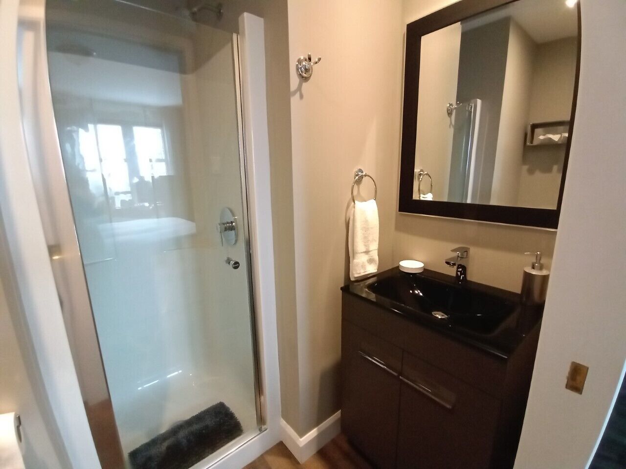 A bathroom with a glass shower enclosure, a dark-toned vanity with a sink, and a mirror above the vanity.
