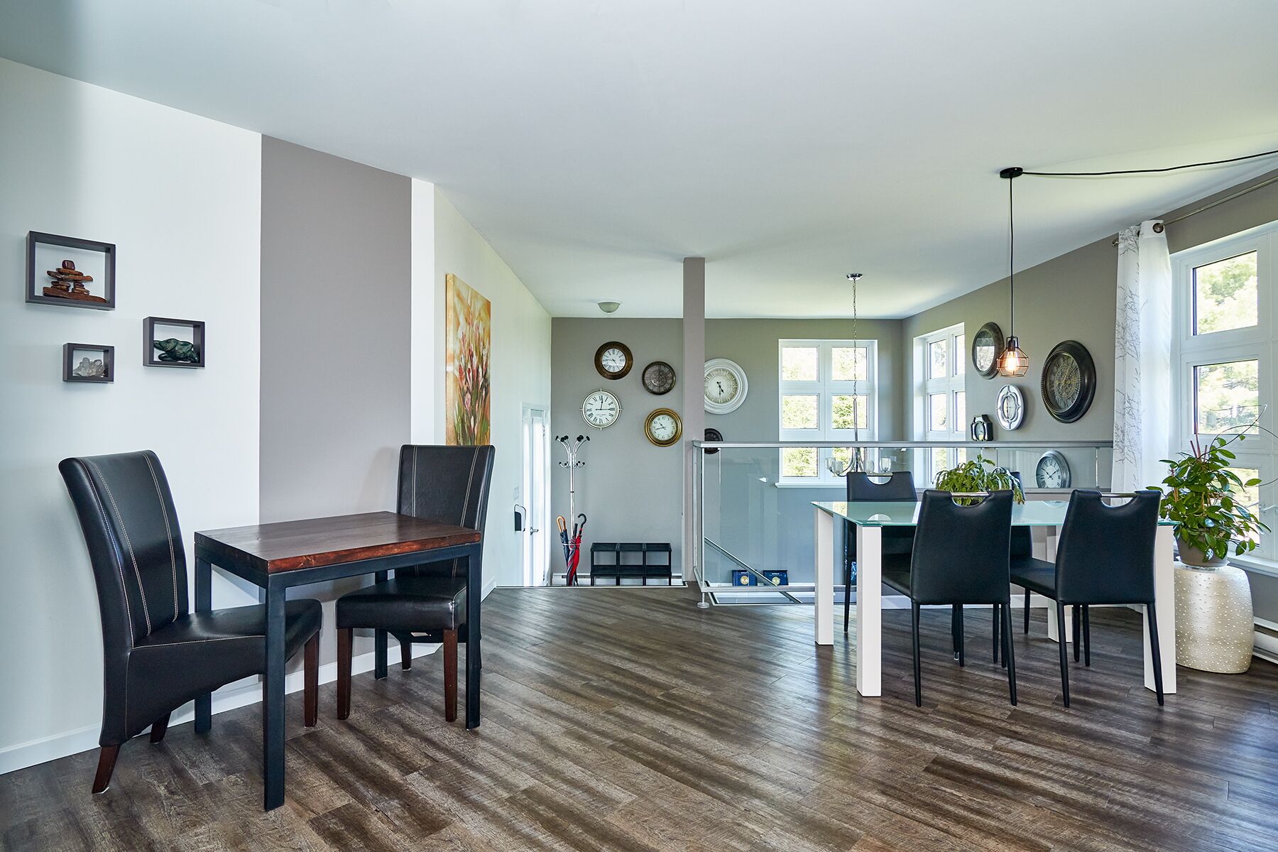A spacious dining area with a wooden table and chairs, a kitchen in the background, and a large window providing natural light.