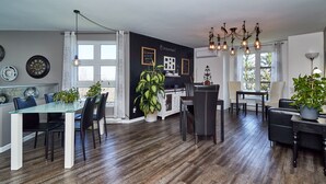 Une cuisine moderne avec un revêtement mural noir, un plancher en bois et un coin repas comprenant une table et des chaises en verre.