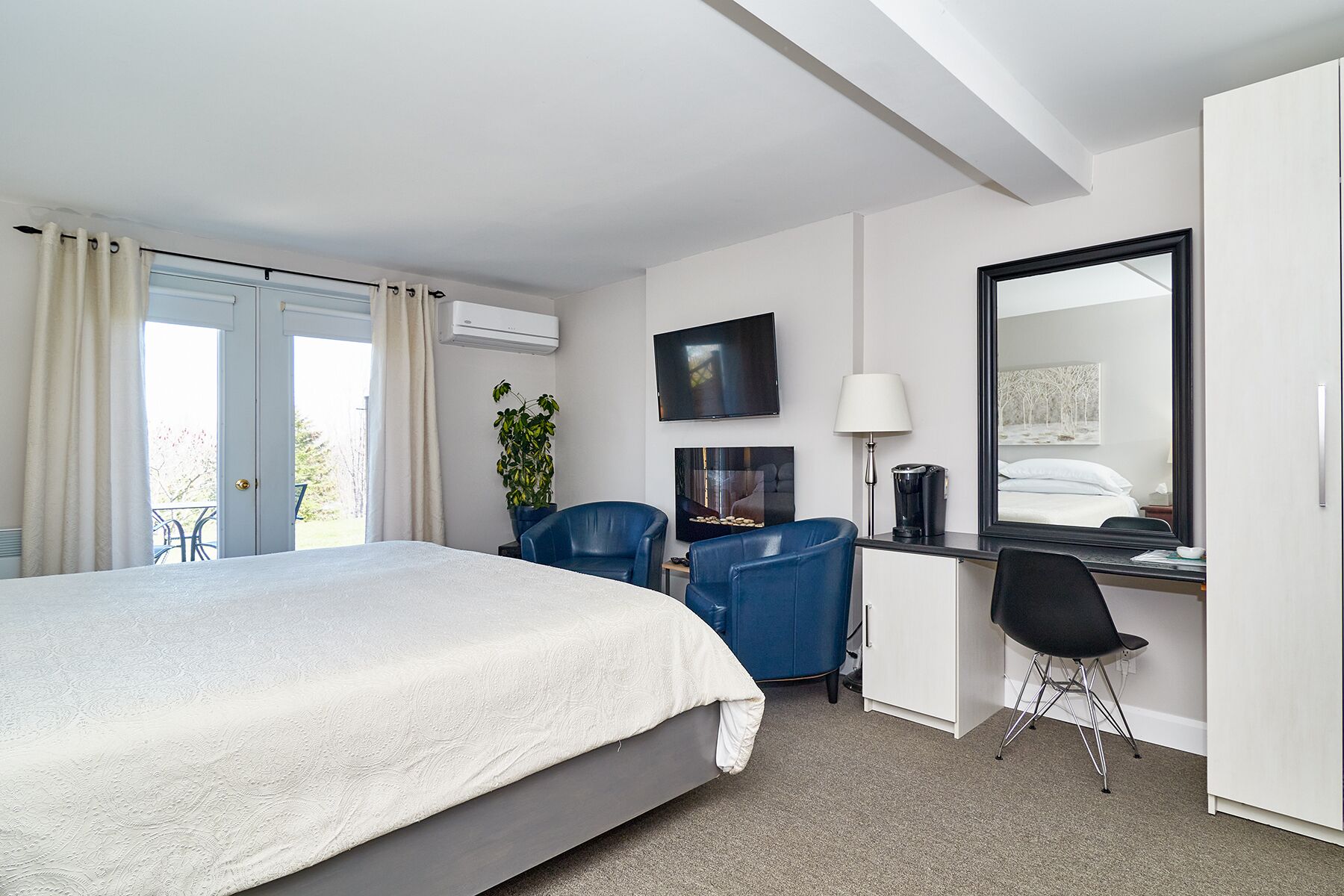 Ein Hotelzimmer mit Bett, Schreibtisch mit Stuhl, Fernseher, Spiegel und einem Fenster mit Vorhängen.