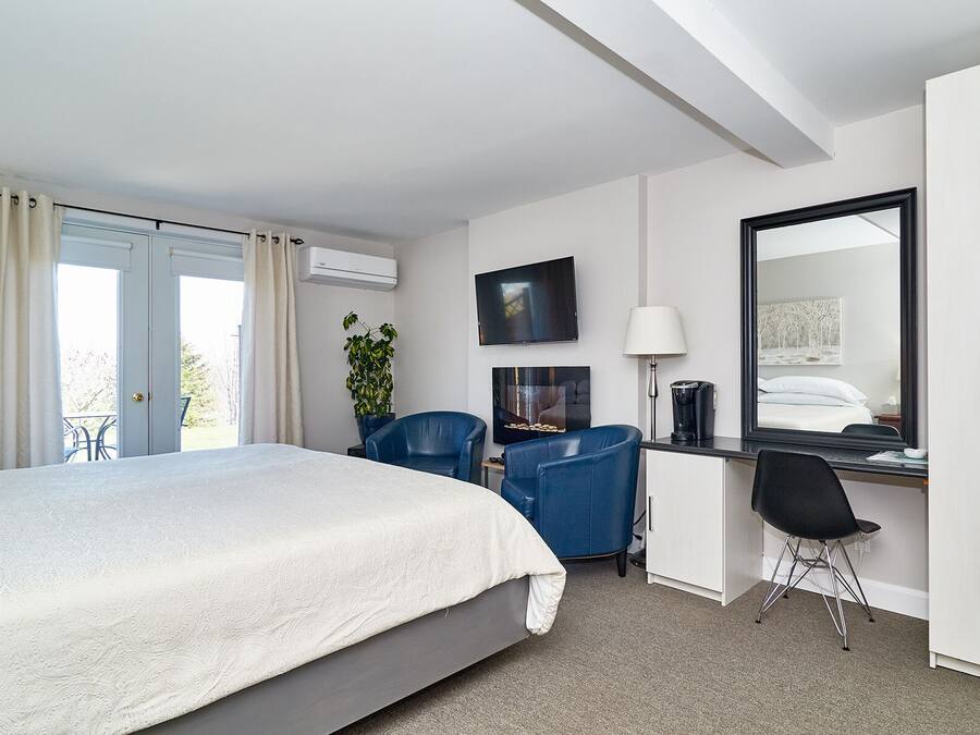 Ein Hotelzimmer mit Bett, Schreibtisch mit Stuhl, Fernseher, Spiegel und einem Fenster mit Vorhängen.