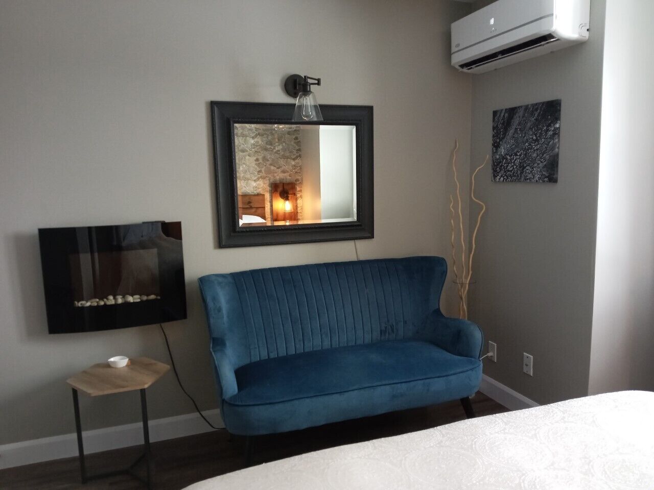 Een moderne slaapkamer met een blauwe bank, een aan de muur bevestigde televisie en een airconditioning.