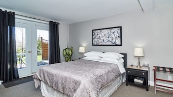 A bedroom with a bed, two bedside lamps, a framed picture on the wall, and a view through a glass door.