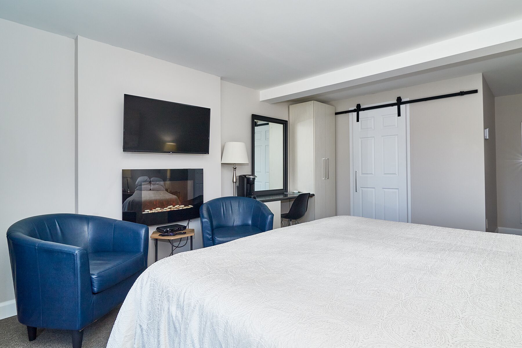 Een hotelkamer met een groot bed, twee blauwe fauteuils, een flatscreen televisie, een bureau met lamp en een kledingkast.