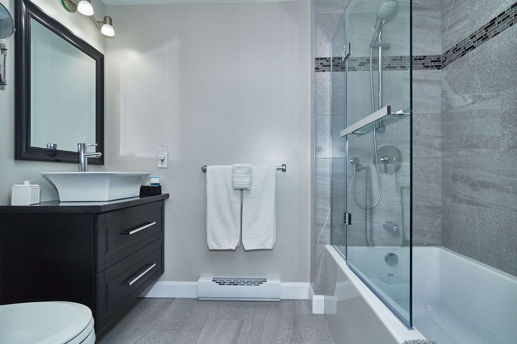 Een moderne badkamer met een douchecabine van glas, een witte wastafel en een donkere badkamerkast.