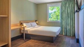 Een hotelkamer met een bed, nachtkastje, raam met gordijnen en een aan de muur bevestigde televisie.