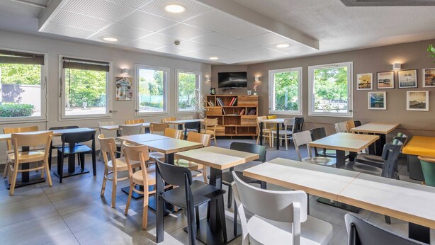 Een ruime kamer met meerdere tafels en stoelen, een boekenkast en een televisie.