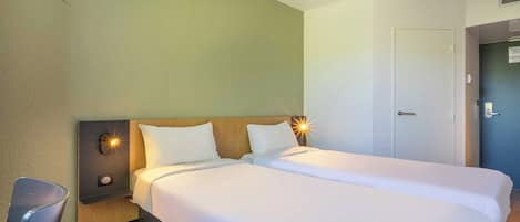 A hotel room with two beds, a desk, and a nightstand with a lamp.