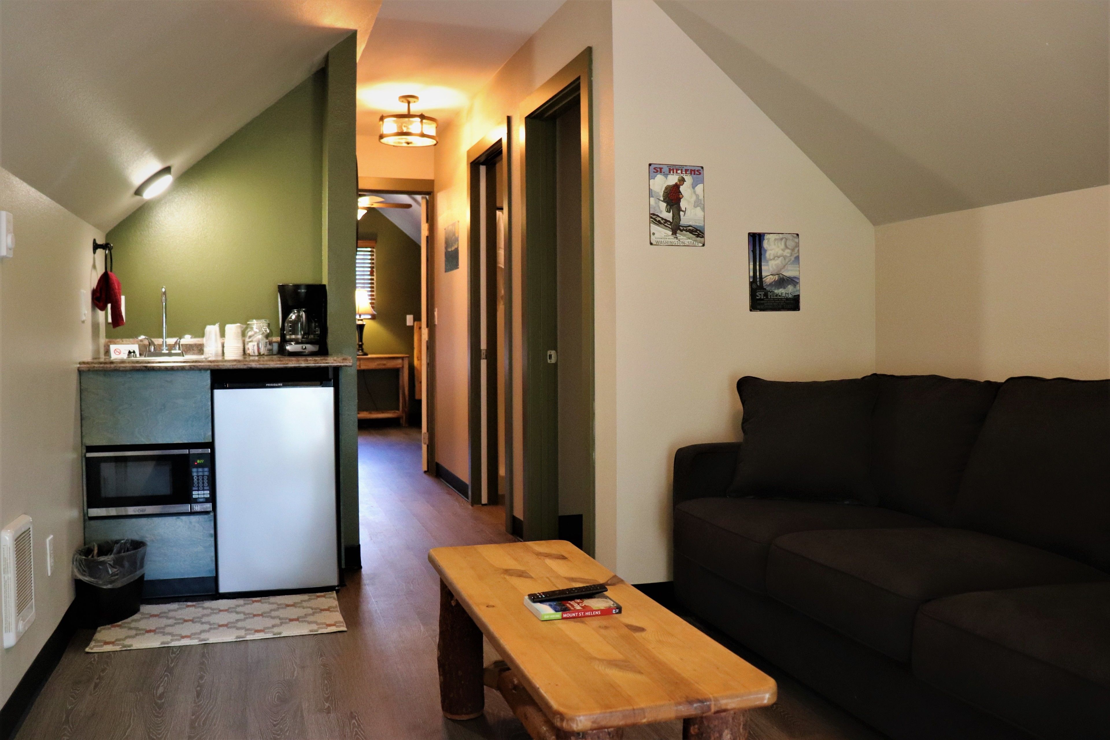A compact living space with a kitchenette, a wooden table, a dark-colored sofa, and a hallway leading to another room.