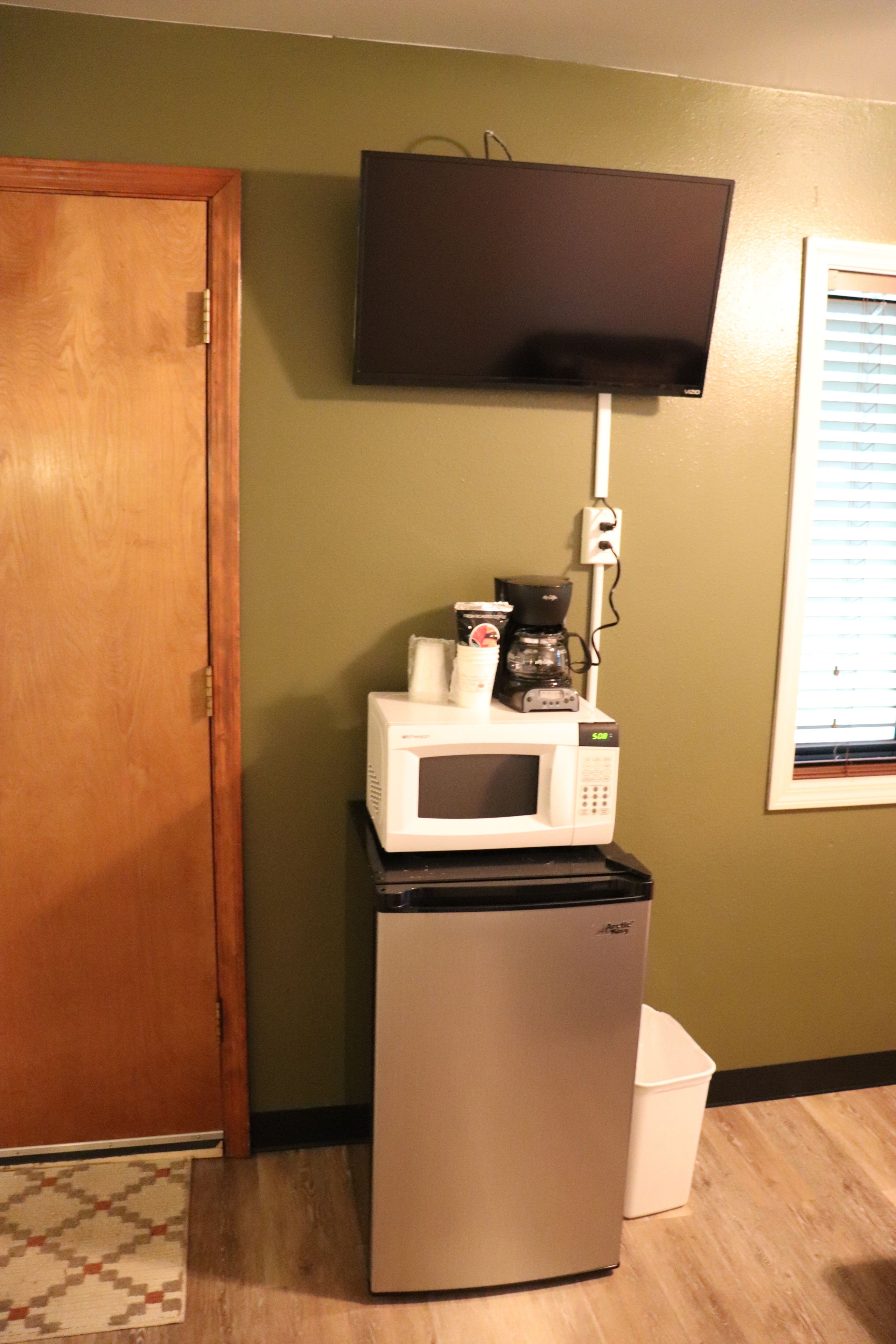 Una kitchenette compacta con microondas, cafetera y refrigerador pequeño.