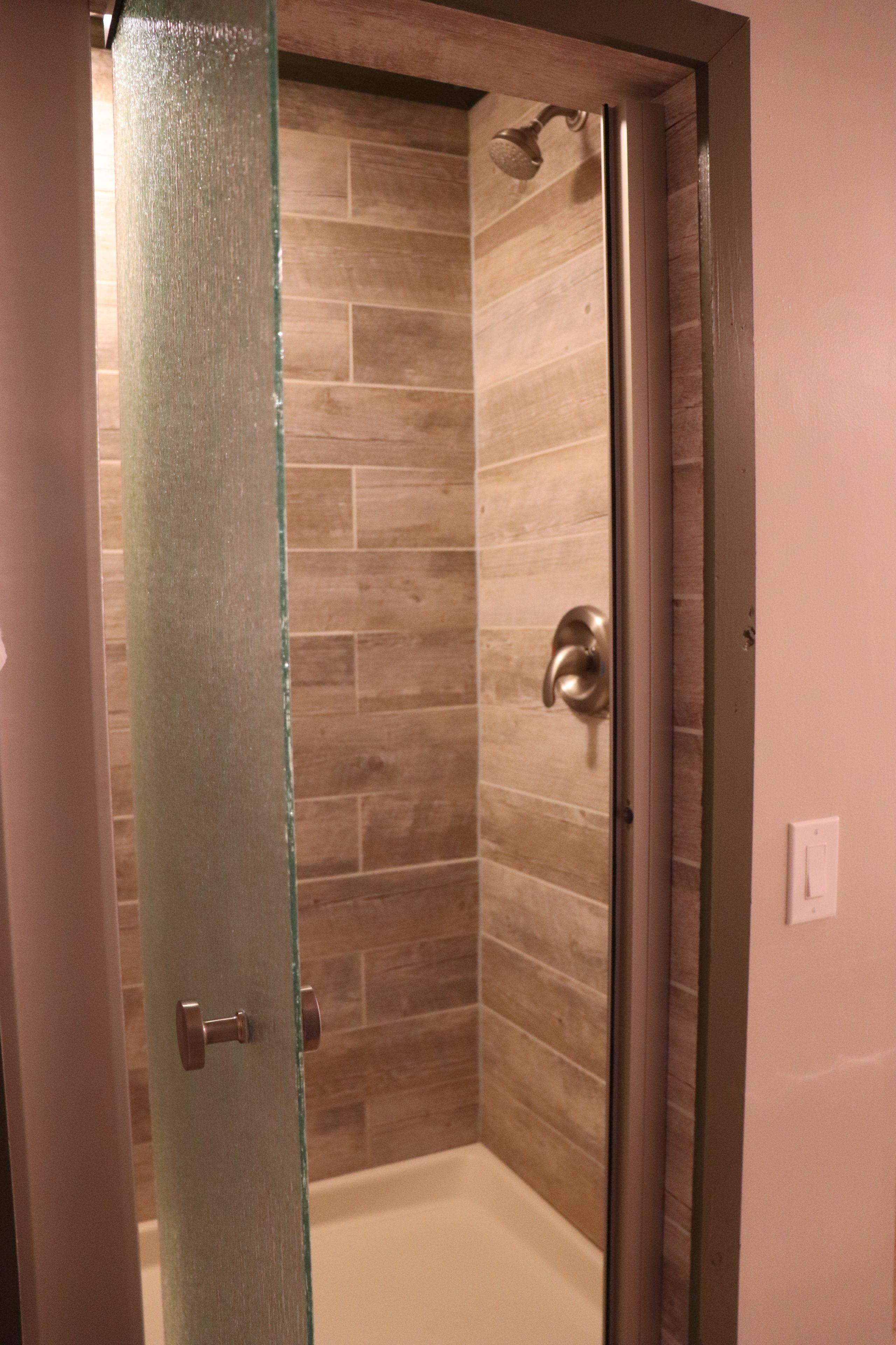A glass door leading to a shower area with a tiled wall and a showerhead.