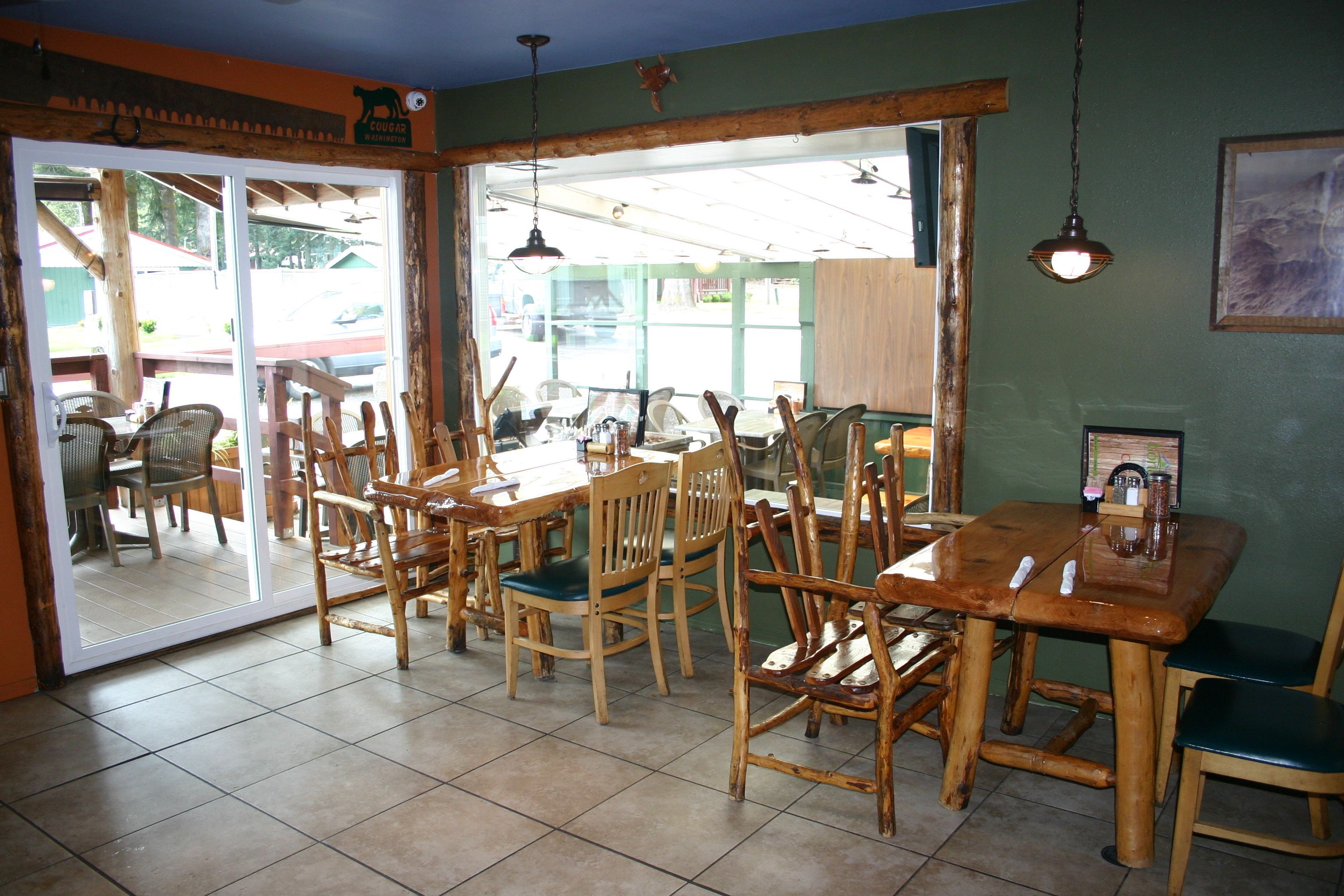 A restaurant interior with wooden tables and chairs, a large window, and a sign on the wall.