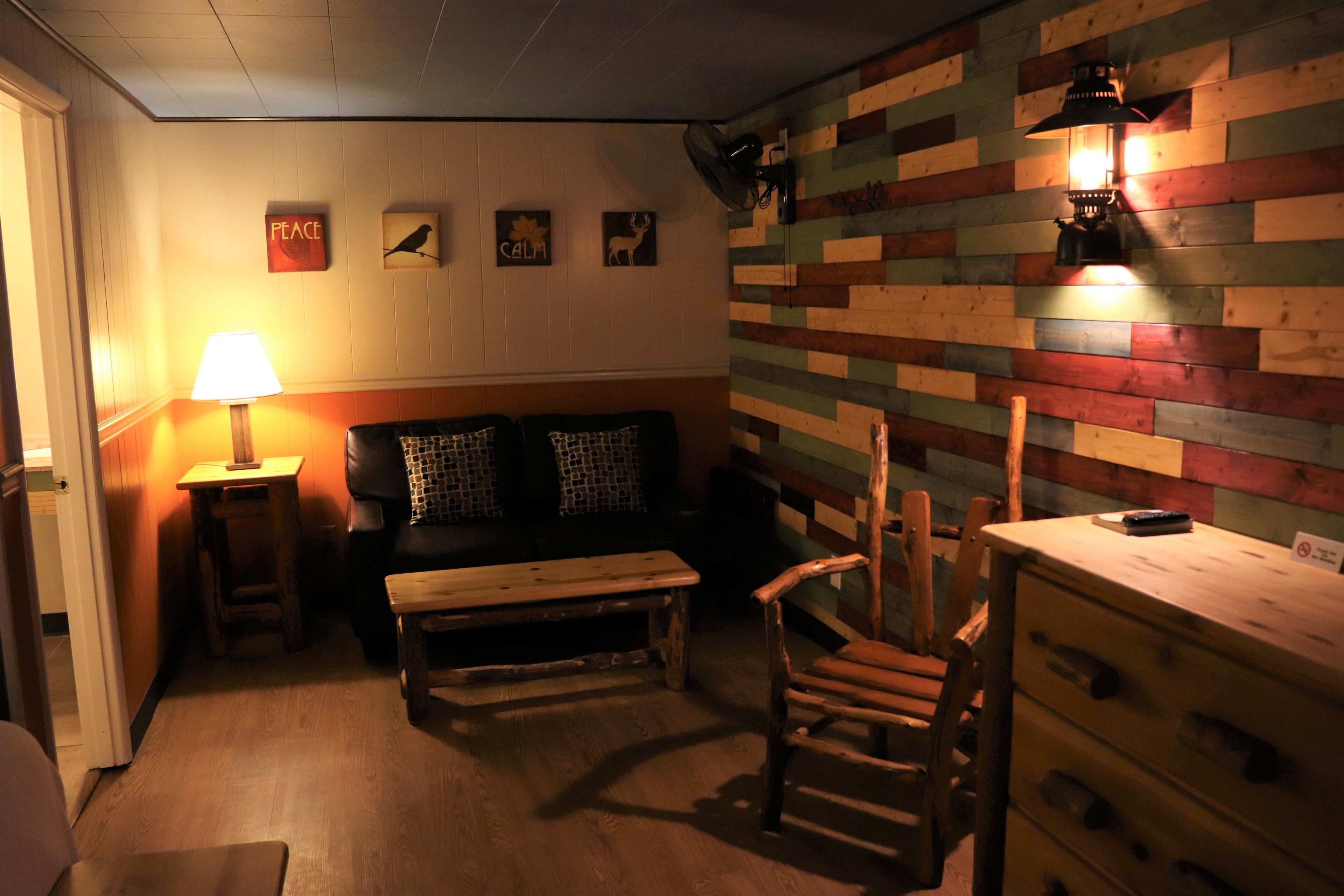 Une pièce chaleureuse avec un banc en bois, une petite table, une chaise et un canapé. Des décorations sont accrochées aux murs et une lampe se trouve sur une table d’appoint.