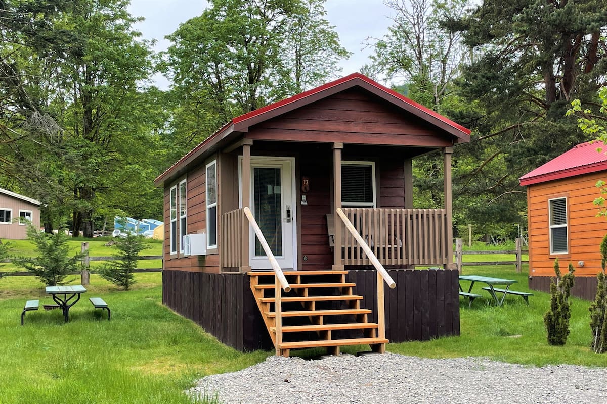 A small wooden cabin with a porch, a set of stairs, and a gravel driveway.