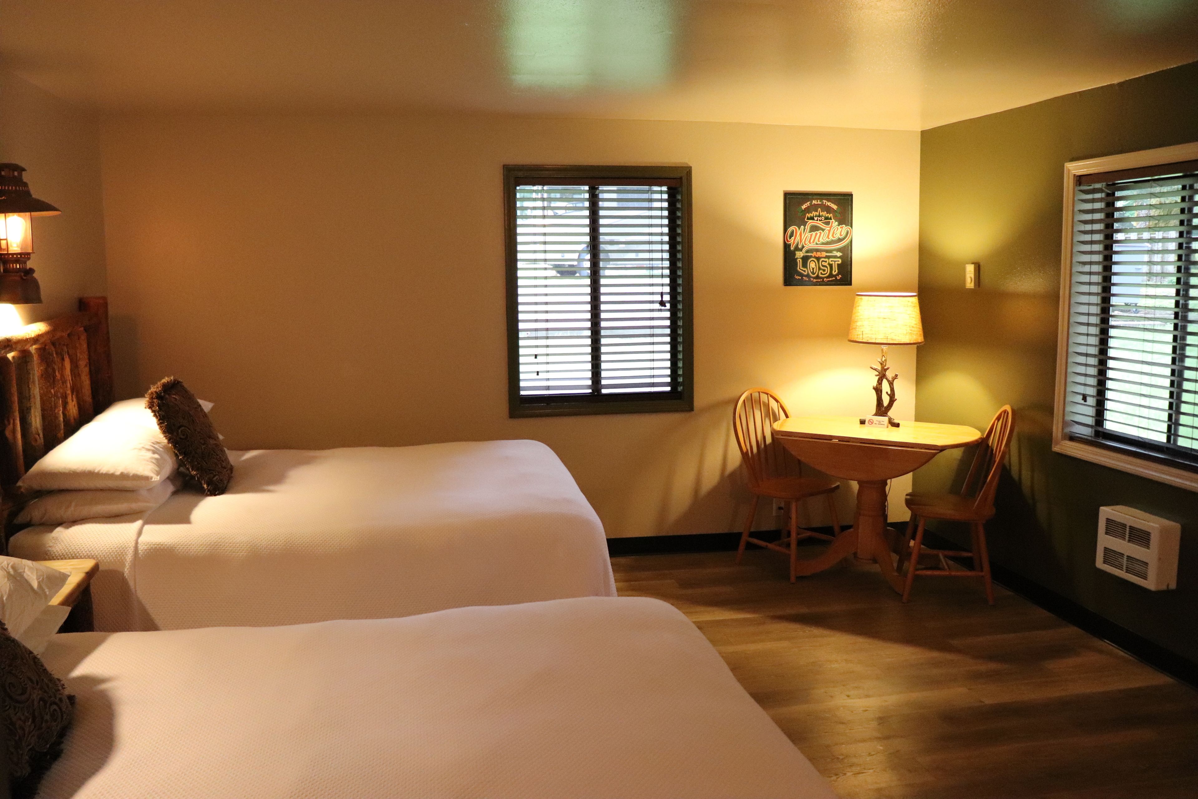 A hotel room with two beds, a small table with chairs, and a window with blinds.