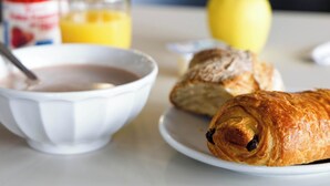 A breakfast setting with a bowl of cereal, a croissant, a glass of orange juice, and a whole apple on a table. - B&B HOTEL Clermont-Ferrand Gerzat 1 (Gerzat)