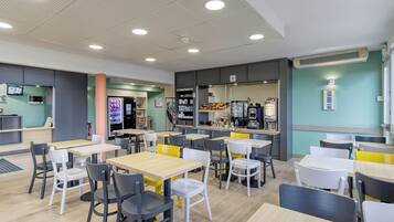 Ein modernes Café mit mehreren Tischen und Stühlen, einer Theke inklusive Speisekarte und einer Kaffeemaschine.