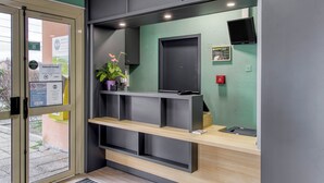 A reception area with a wooden counter, a black door, and a green wall. - B&B HOTEL Clermont-Ferrand Gerzat 1 (Gerzat)