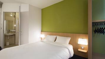 Habitación de hotel con cama, mesita de noche con lámpara, pared de acento verde y baño visible a través de una puerta abierta.