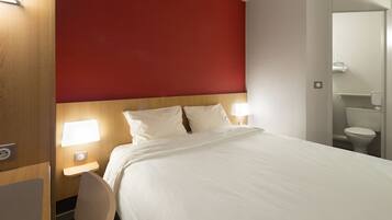 A hotel room with a large bed, bedside lamps, a wooden headboard, and a red accent wall.