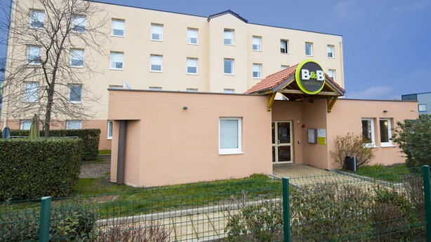 A B&B hotel with a beige facade, multiple windows, and a green fence in the foreground. - B&B HOTEL Clermont-Ferrand Gerzat 1 (Gerzat)
