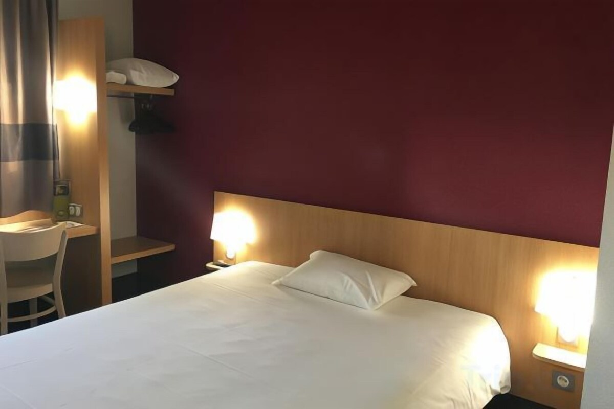 Una habitació d'hotel amb un llit, làmperes de nit, una escriptori i una cadira.