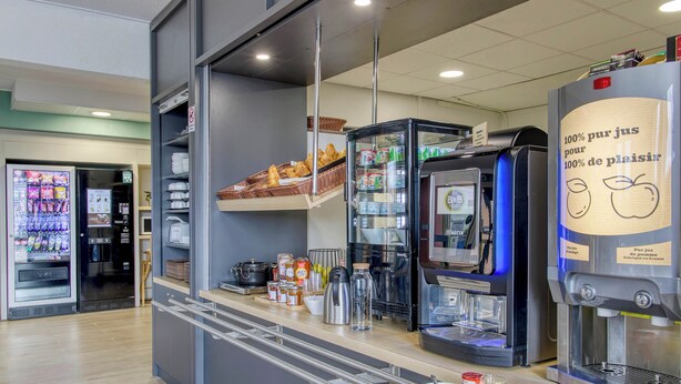 Un café moderno con una máquina de café automática, varias opciones de productos de panadería y un dispensador de bebidas.