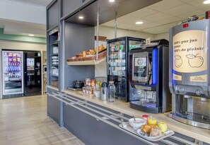 A modern café with a self-service coffee machine, a variety of baked goods, and a beverage dispenser. - B&B HOTEL Clermont-Ferrand Gerzat 1 (Gerzat)