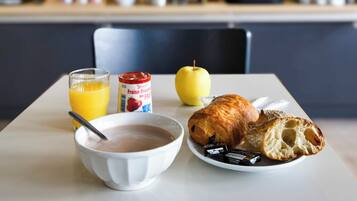 A breakfast table with a bowl of cereal, a glass of orange juice, a croissant, and an apple.