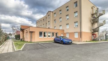 Un edificio residencial de varios pisos con un coche azul estacionado en la entrada.