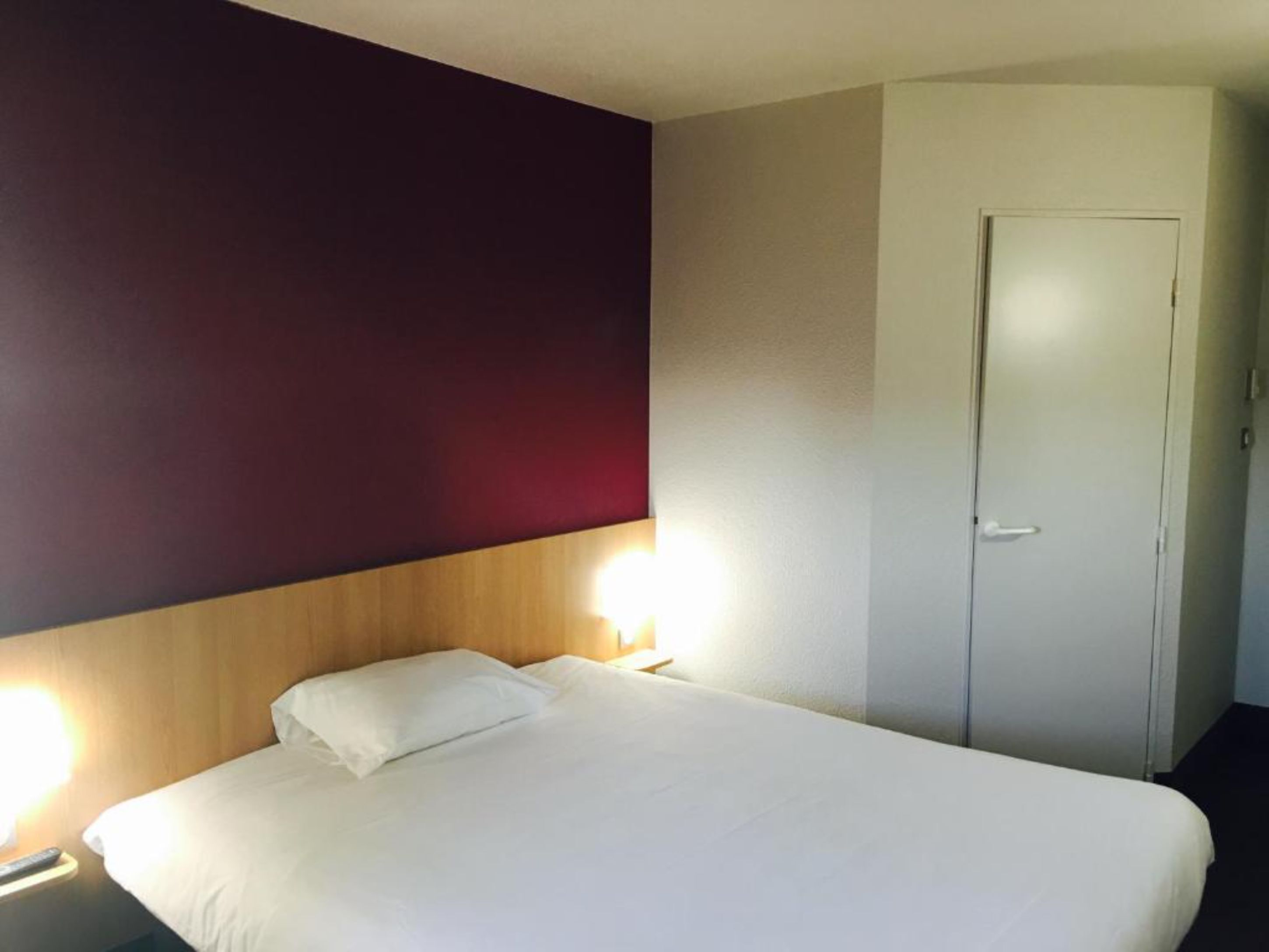 A hotel room with a bed, a nightstand, and a door.