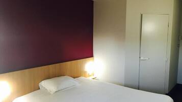 A hotel room with a bed, a nightstand, and a door.