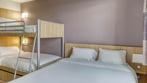 Habitación de hotel con una litera, una cama individual, cabecera de madera, mesita de noche con lámpara y luz de pared.
