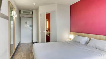 Een hotelkamer met een bed, een deur naar een badkamer en een rode accentmuur.