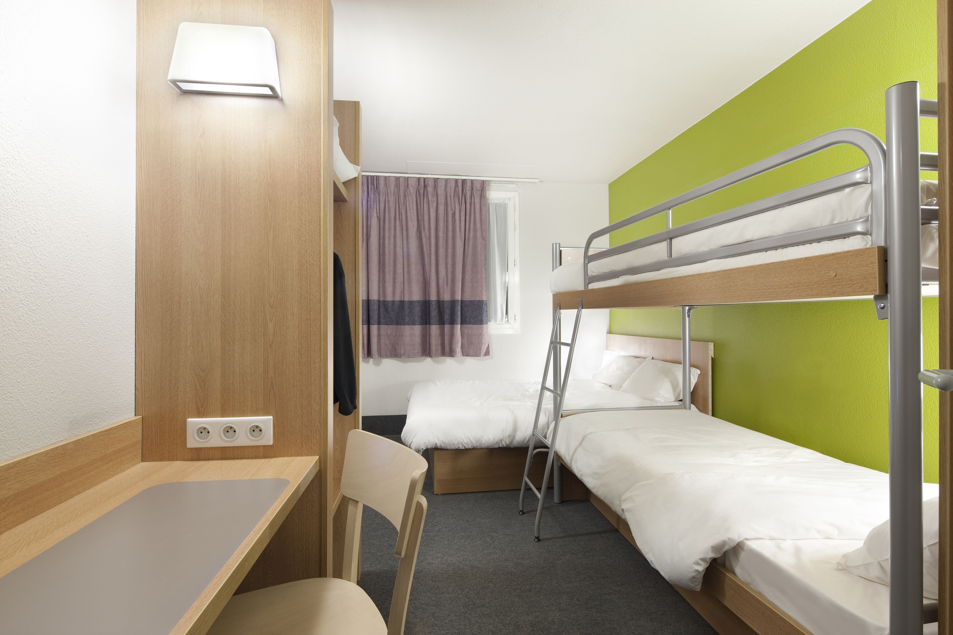A compact hotel room with bunk beds, a desk, and a chair.