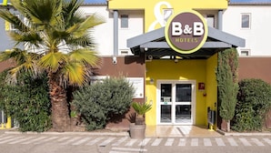 A B&B hotel with a yellow facade, palm trees, and a signboard. - B&B HOTEL Avignon (2) (Le Pontet)