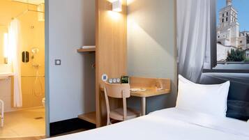 Habitación de hotel con cama, escritorio, ducha y vista a un edificio histórico.