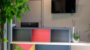 A reception desk with a laptop, a television, and a plant in a vase. - B&B HOTEL Avignon (2) (Le Pontet)