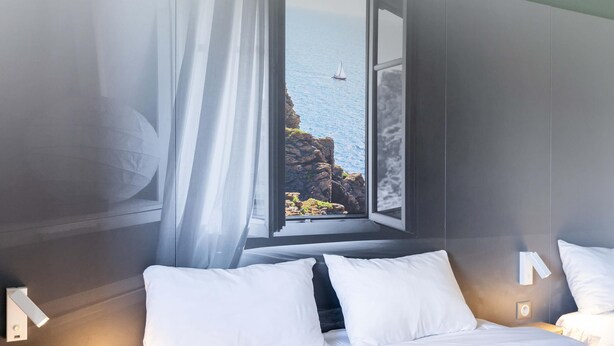 A hotel room with a bed, a window with a view of the sea, and a curtain.
