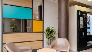 A modern lobby with two leather chairs, a small round table, a plant, and a vending machine.