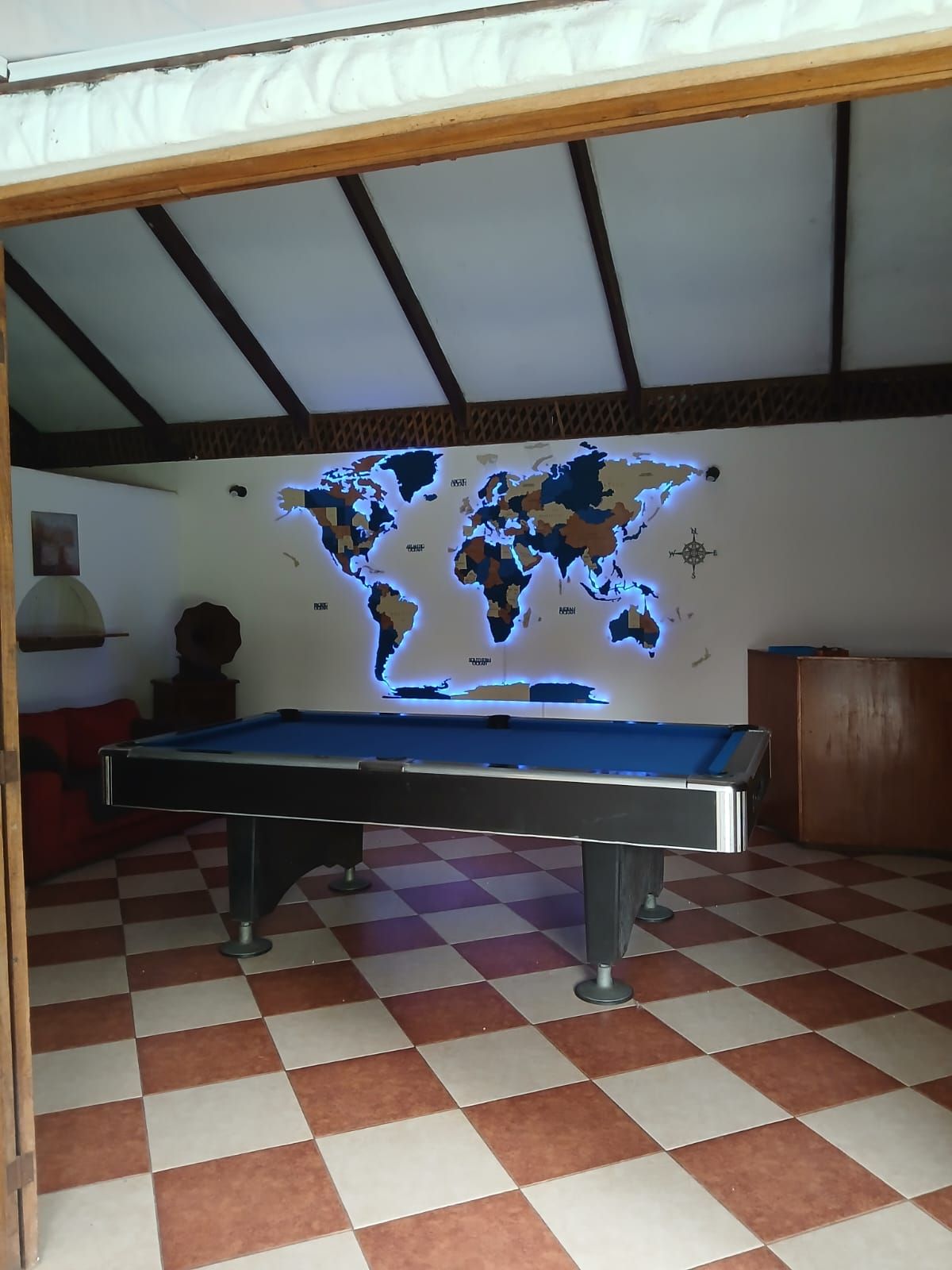 A pool table with a world map projection, checkered floor, and wooden ceiling beams.