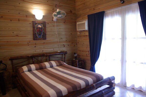 Una habitación de cabaña de madera con una cama, un ventilador y una ventana con cortinas.