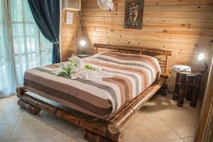 Una cama de madera con una colcha a rayas, una mesita de noche con una lámpara y un aire acondicionado fijado a la pared.