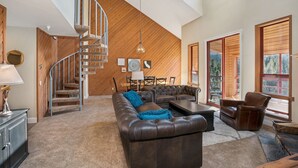 A spacious living room with a brown leather sofa, a coffee table, and a fireplace. A wooden staircase leads to an upper level.