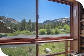 A window view of a mountainous landscape with a road, a building, and a green truck.