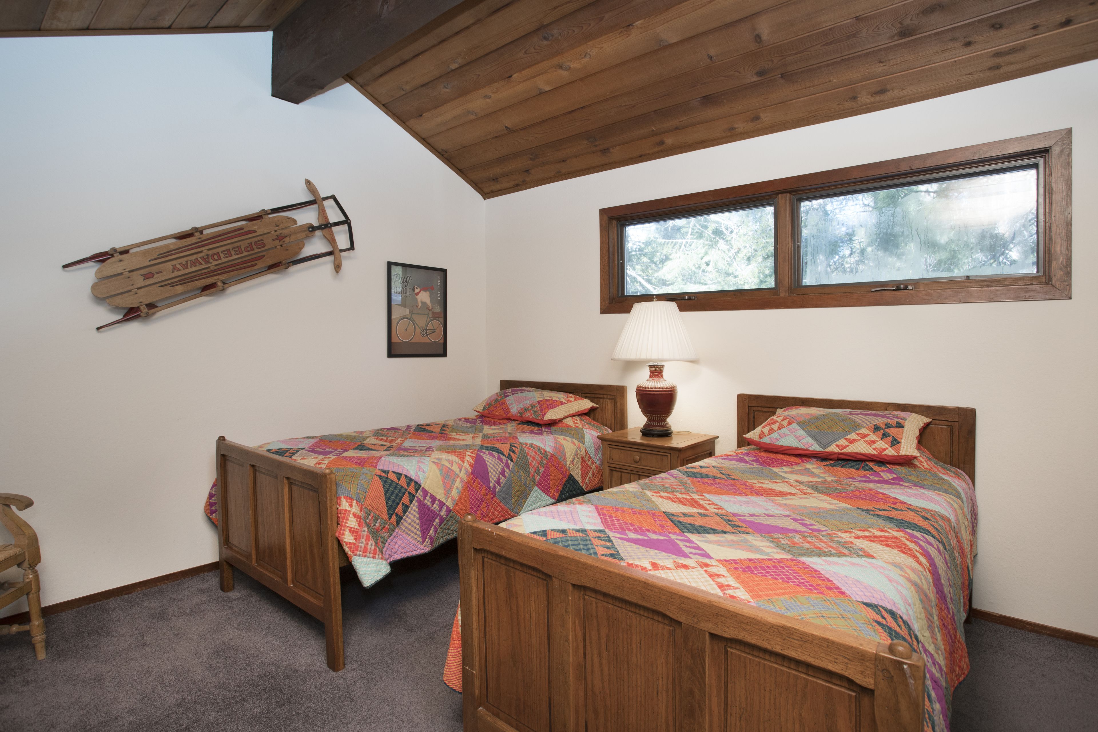 A room with two wooden beds, a wooden ceiling, a window, and a wooden sled on the wall.