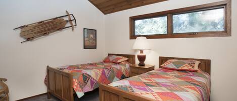 A room with two wooden beds, a wooden ceiling, a window, and a wooden sled on the wall.