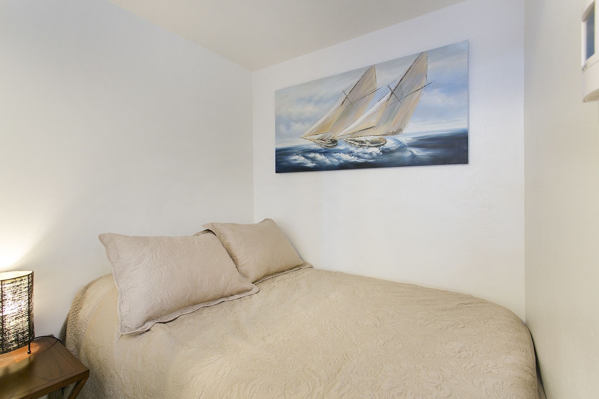 A bedroom with a bed, a nightstand, a lamp, and a painting of a sailboat on the wall.